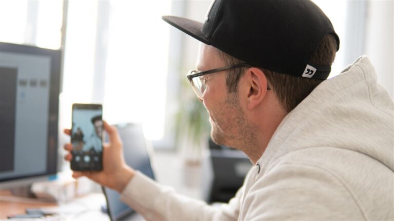 Mitarbeiter prüft eine Unternehmensdarstellung auf dem Smartphone am Schreibtisch
